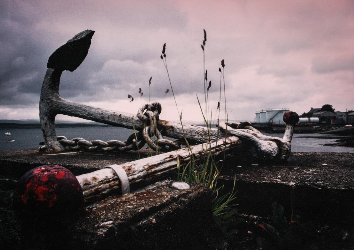 A weathered harbour anchor and chain beneath a pink-grey sky