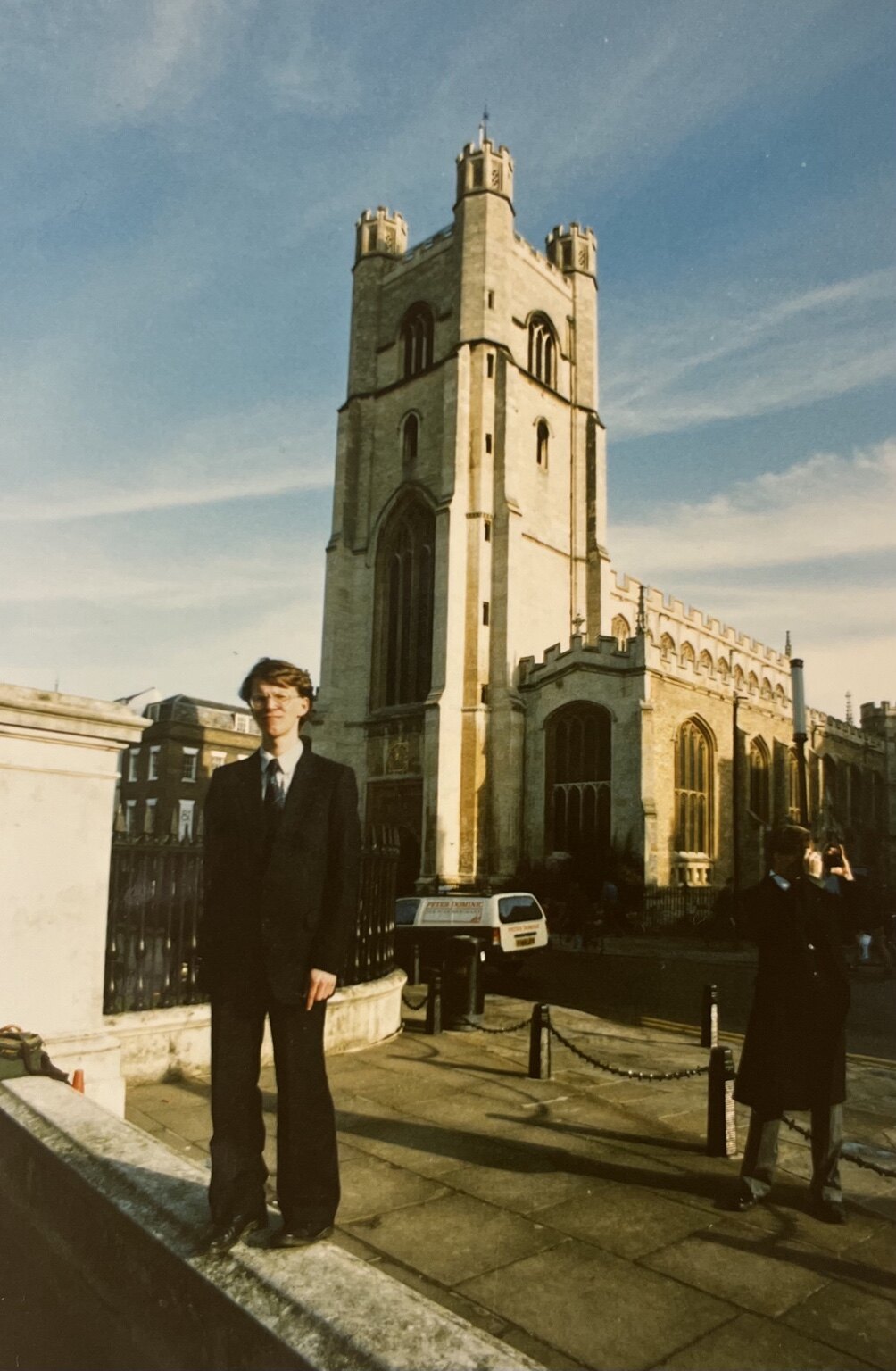 A suited figure standing in front of a tall stone church tower