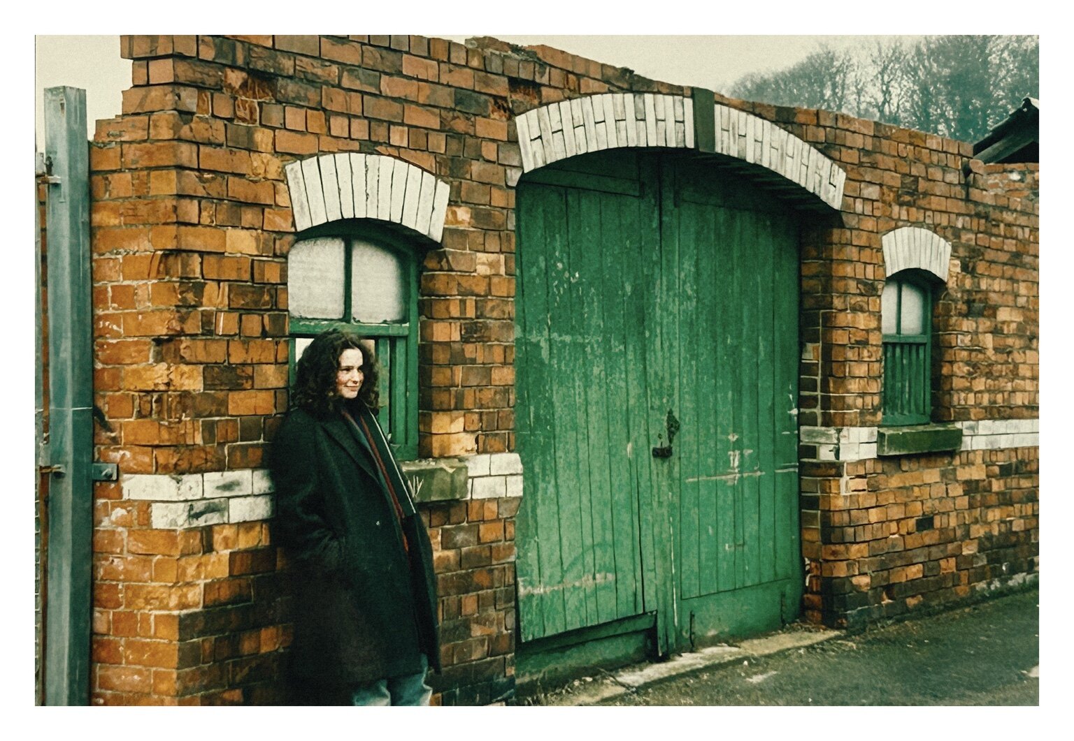 A woman standing beside a large weathered green door in a brick wall